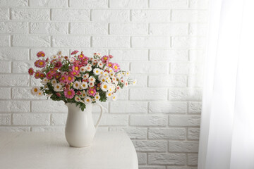 Vase with beautiful flowers on wooden table near white brick wall. Space for text