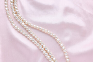 Elegant pearl necklace on pink fabric, top view. Space for text