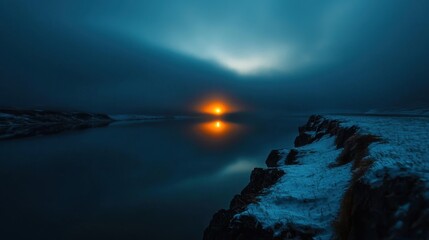 Golden sunlight casts a warm glow on a quiet lake, with dark clouds hovering overhead and rocky shores edged in light snow. A peaceful moment in nature as night approaches