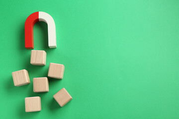 Magnet attracting wooden cubes on green background, flat lay. Space for text