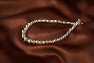 Beautiful pearl necklace on brown silky fabric