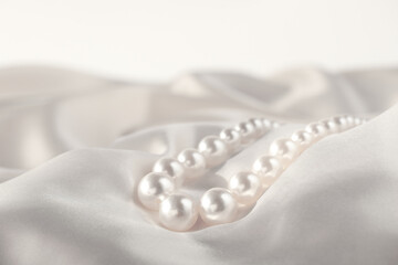 Beautiful pearl necklace on white silk, closeup