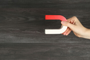 Woman with horseshoe magnet on wooden background, closeup. Space for text