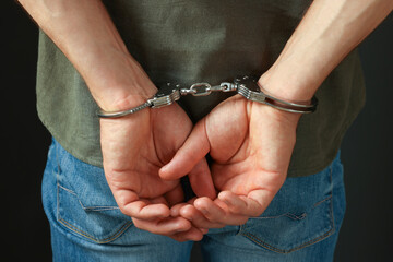 Man in metal handcuffs on black background, back view