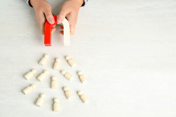 Man with magnet attracting wooden human figures at light table, above view. Space for text