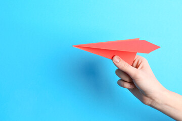 Woman with handmade paper plane on light blue background, closeup. Space for text