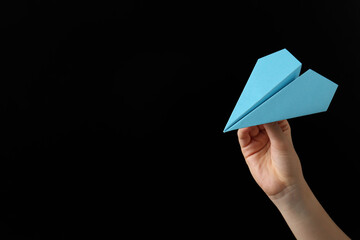 Woman with light blue paper plane on black background, closeup. Space for text