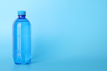 Plastic bottle of water on light blue background. Space for text