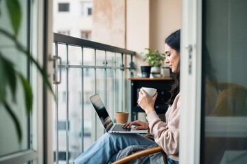 Woman working on laptop while sitting by balcony at home