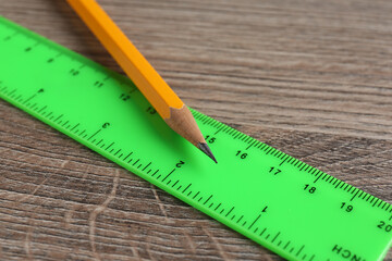 Green ruler and pencil on wooden table, closeup