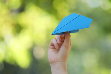 Woman with handmade paper plane on blurred green background, closeup. Space for text