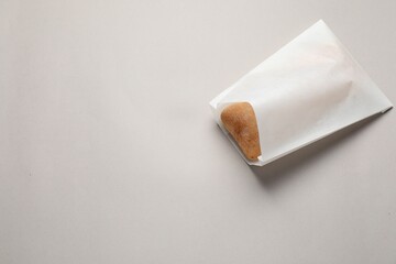 Paper bag with fresh ciabatta on beige background, top view. Space for text