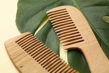 Wooden combs and monstera leaf on beige background, closeup