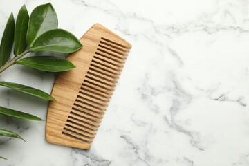 Wooden comb and branch with leaves on white marble table, flat lay. Space for text
