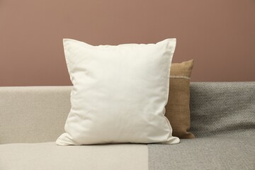 Blank soft pillow on cozy couch against brown background