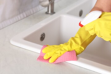 Woman using cleaning product while wiping sink with rag in kitchen, closeup
