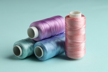 Different spools of sewing threads on light blue background, closeup