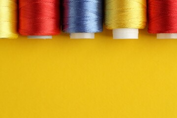 Different spools of sewing threads on yellow background, flat lay. Space for text