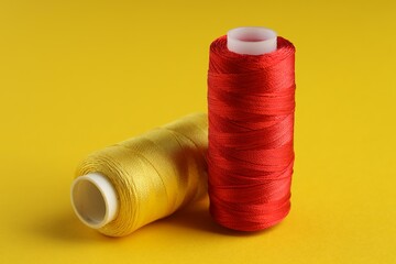 Different spools of sewing threads on yellow background, closeup