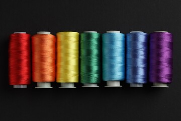 Different spools of sewing threads on black background, flat lay