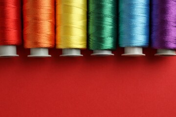 Different spools of sewing threads on red background, flat lay. Space for text