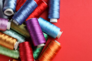 Different spools of sewing threads on red background, flat lay. Space for text