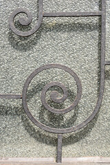 A metal railing with decorative spiral elements in front of a textured glass surface