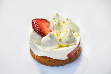 A mini dessert cake featuring strawberries, white cream, and sprinkles stands out against a white background