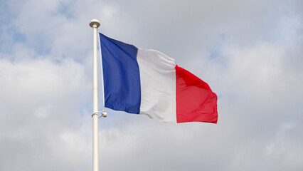 French national flag waving on cloudy sky background. The flag on a flagpole flutters in the wind. The image conveys the spirit of France: freedom, equality, fraternity.