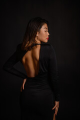 Fototapeta premium A portrait of a beautiful Asian woman in an open black dress, with red lipstick on her lips, exuding elegance, confidence, and timeless beauty