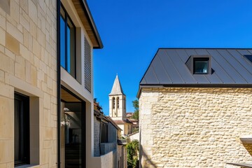 Obraz premium Charming architectural view revealing rustic buildings and a historic church tower under a bright blue sky in a quaint village setting