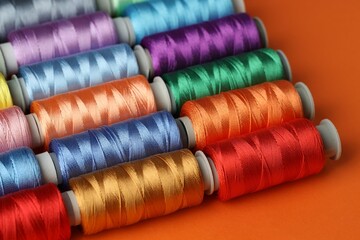 Different spools of sewing threads on orange background, closeup