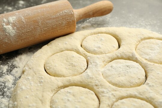 Raw dough and rolling pin on grey table, closeup