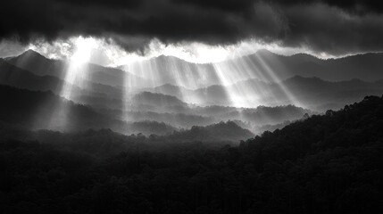 Sunbeams break through dark clouds over a mountainous landscape.