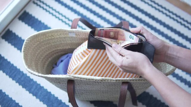Woman packing straw bag for beach, cosmetics, money purse and beach towel