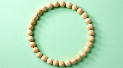 A circular arrangement of light beige wooden beads on a pale green background creates a simple yet elegant frame.