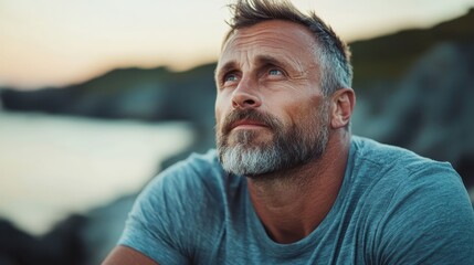 A thoughtful man with a beard sits on the edge of the shore, reflecting on life as the sunset casts a beautiful glow over the tranquil water, embodying peace and contemplation.
