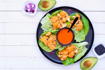 Plate of healthy lettuce wraps with buffalo flavor grilled cauliflower. Top view table scene over a white wood background. Plant-based diet concept.