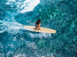 Woman rides on longboard on ocean wave. Drone view of woman during surfing in tropics
