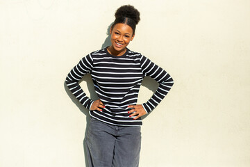 Young African American woman smiling with hands on hips against a beige wall