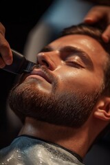 Young man receives beard trim in barbershop. Skilled hairdresser expertly trims beard using electric razor. Relaxed client sits comfortably stylist works. Modern barber shop atmosphere. Stylish