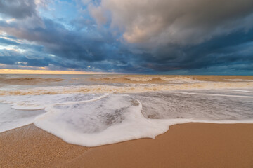 Sandy sea shore during the sunset and stormy weather.