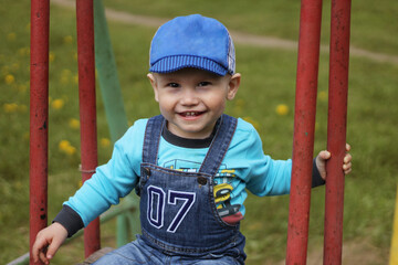 Smiling young boy in a blue cap playing on playground equipment against a grassy background
