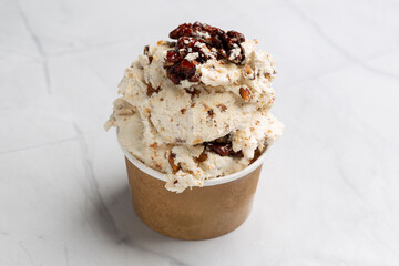 Smooth butter pecan ice cream topped with caramelized pecans spilling from disposable cup onto marble surface
