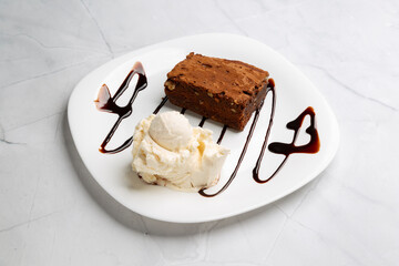 Chocolate brownie featuring smooth vanilla ice cream, generously drizzled with decadent chocolate syrup, presenting irresistible sweet indulgence