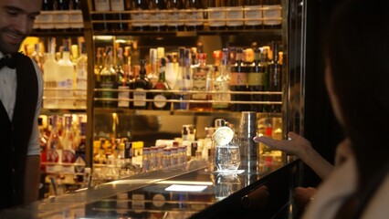 Portrait of VIP guest in beautiful woman making a toast in cheers at luxurious nightclub at vibrant nightlife party. Sitting at counter bar talking with barman atmosphere party lifestyle. Vinosity.