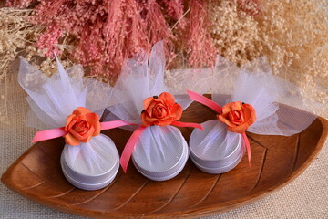 Wedding favors wrapped round gift boxes, white orange pink silver color, lip balms guest souvenirs, ribbon bow flower, beautiful packaging presents for party event guest, wooden plate background
