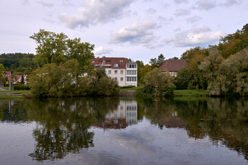 Fototapeta premium Tranquil European Riverside Village at Dusk: Picturesque Houses Nestled Among Lush Greenery Under Dramatic Evening Sky