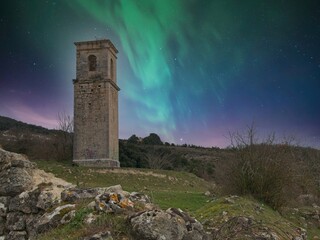 Church tower in haunted village Ochate under the night sky with northern lights, in Treviño, Burgos, Spain