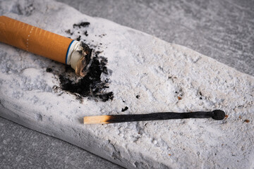 Cigarette butt and burnt match on grey background, closeup.